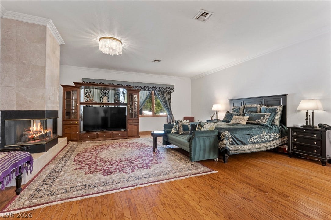 Rich hardwood flooring and a warm corner fireplace anchor this spacious main bedroom suite.