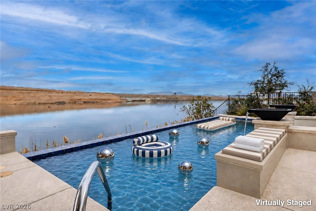 An infinity pool overlooks calm waterfront views under blue skies.