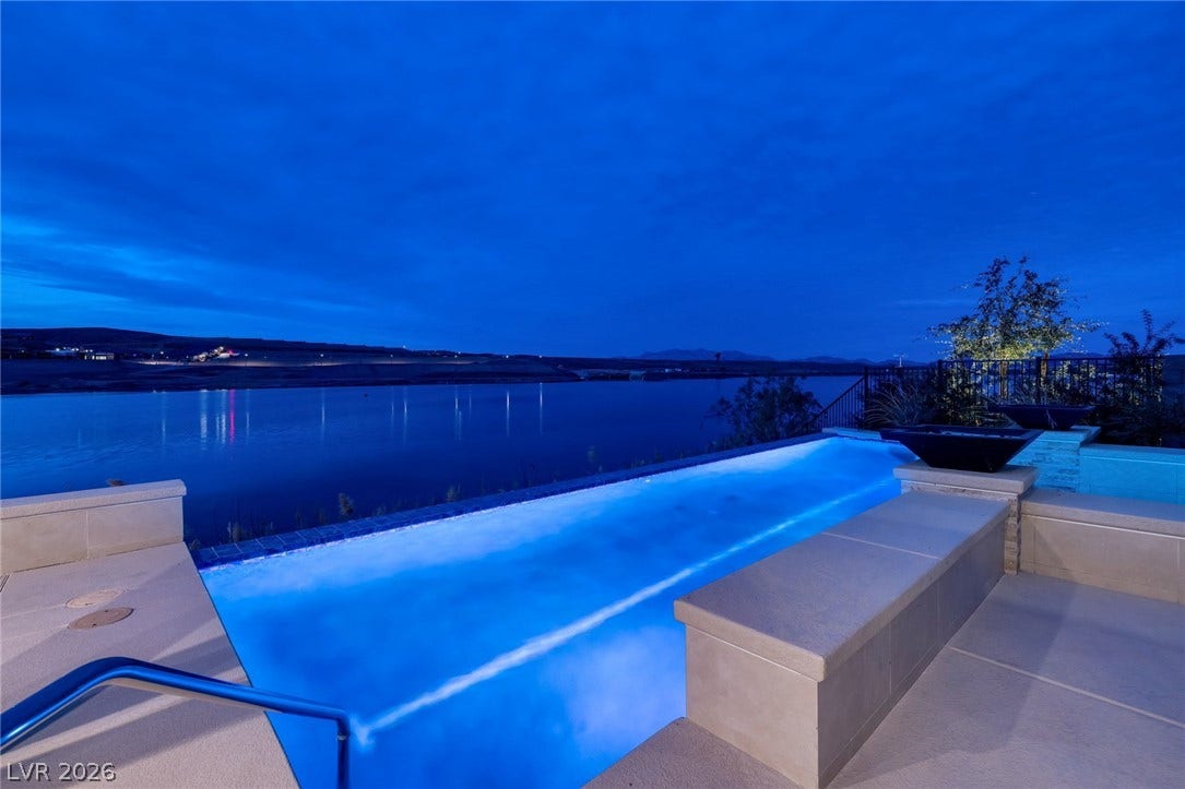 An illuminated infinity pool overlooks a serene body of water under a twilight sky.