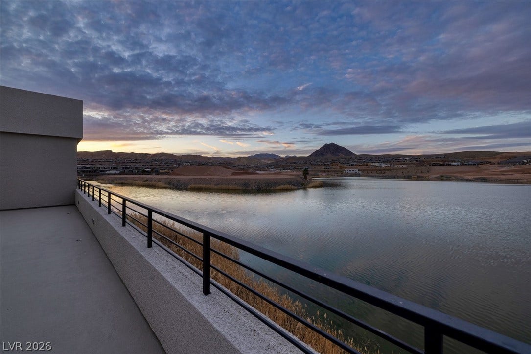 An elevated terrace overlooks peaceful waters and distant mountains under a dramatic twilight sky.