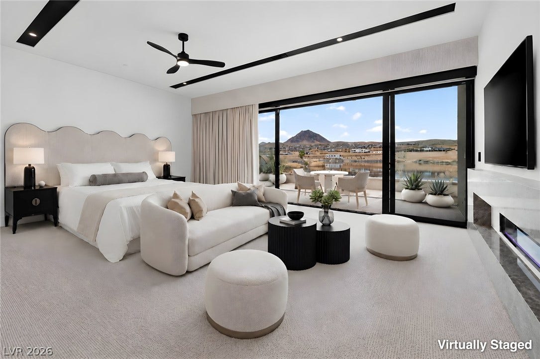 Sliding glass doors frame picturesque water and mountain vistas from this spacious primary suite.