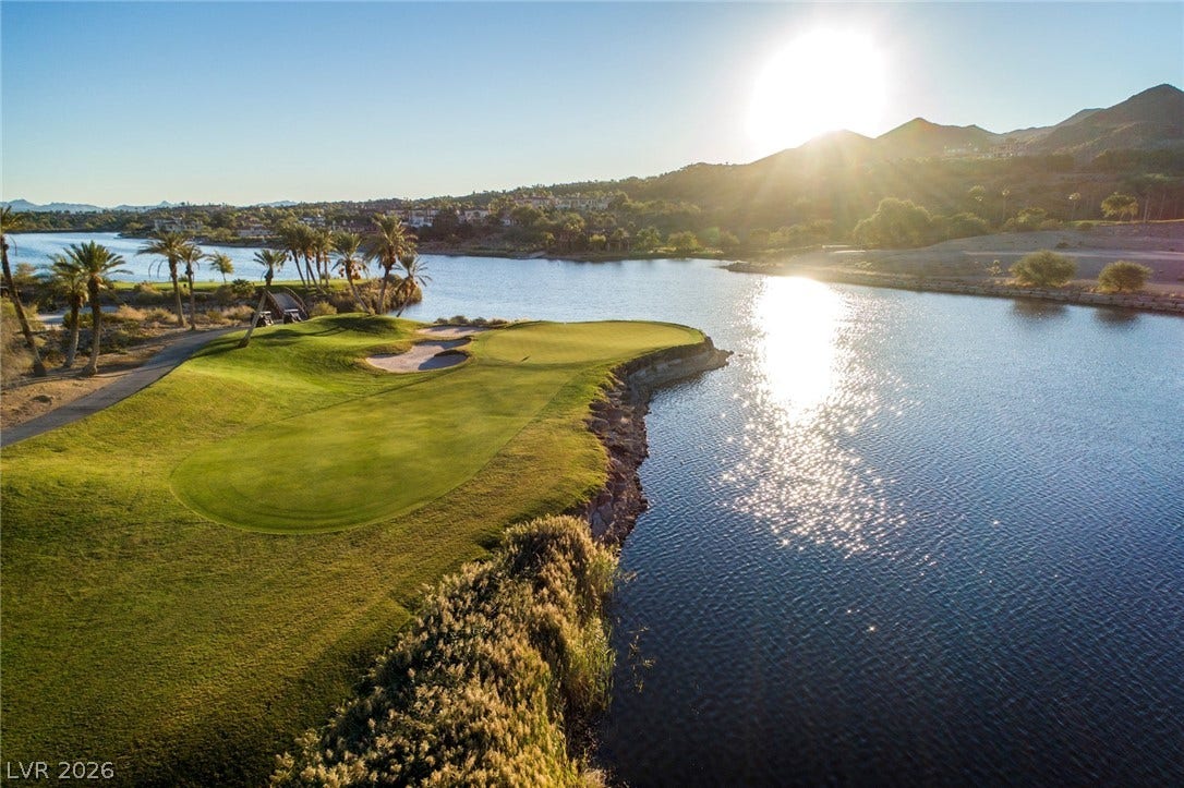 A pristine fairway meets the tranquil water under a brilliant mountain sunset.