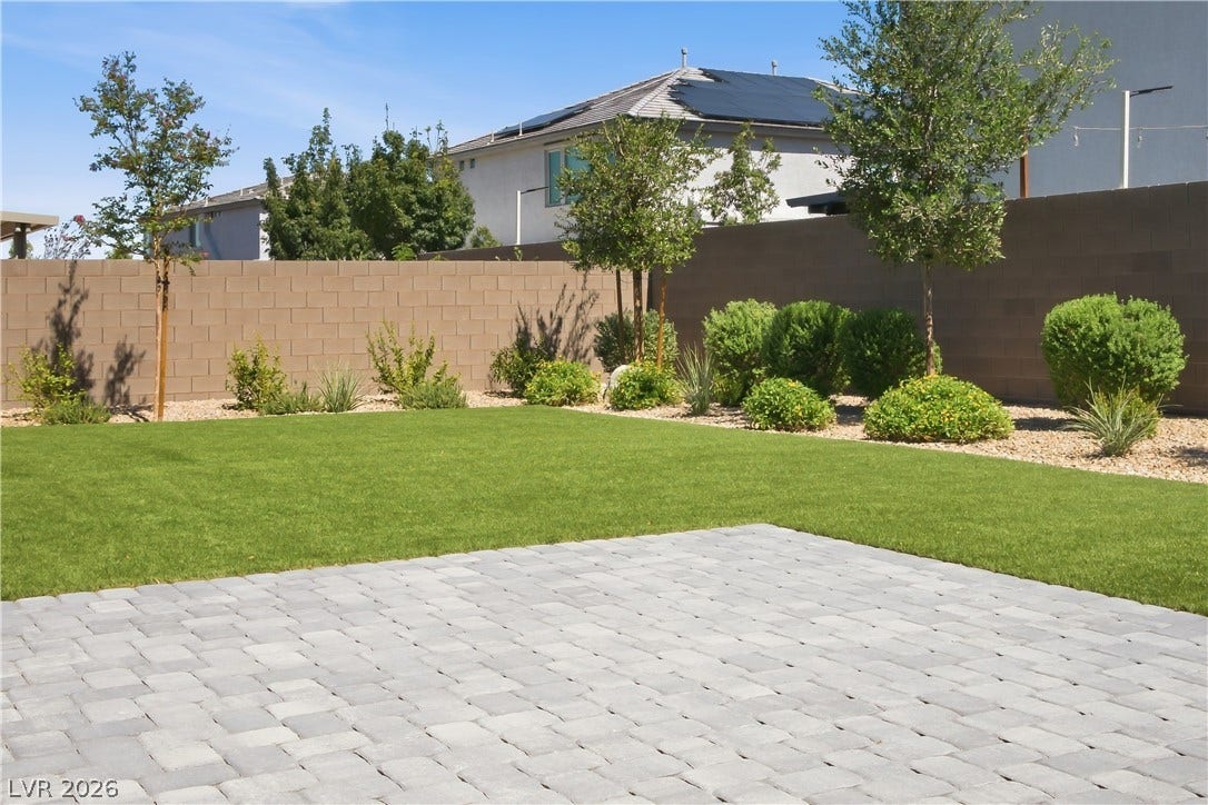 11164 Twisty Ridge Street, Las Vegas, NV 89183 A stone paver patio overlooks a manicured green lawn enclosed by tall privacy block walls.