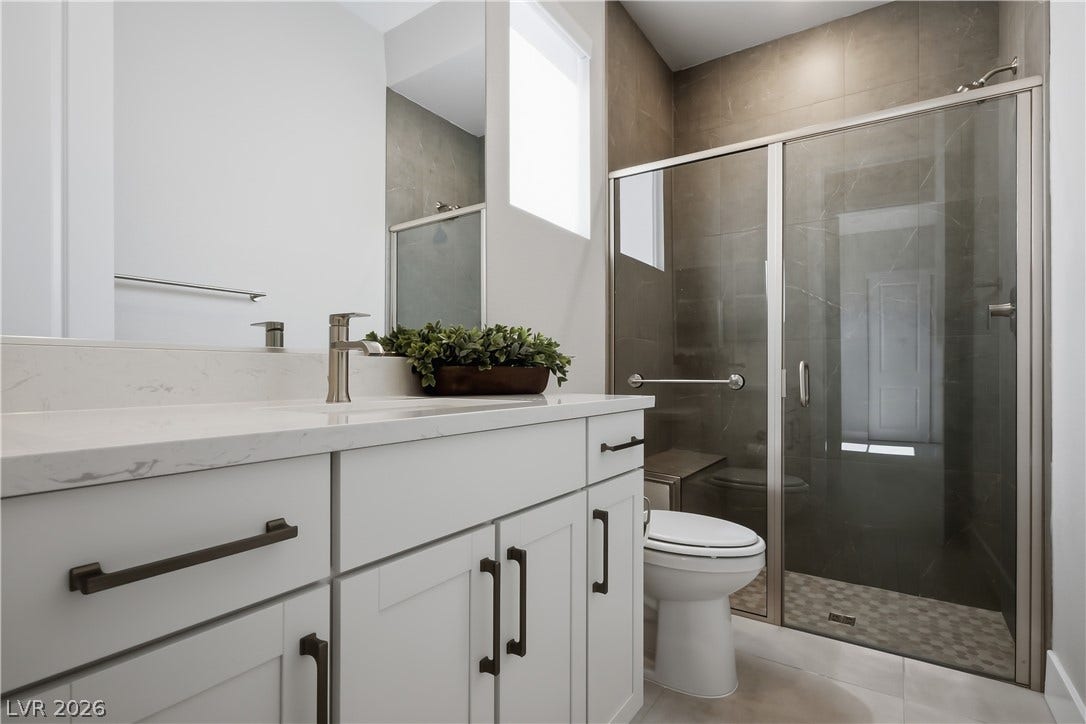 11164 Twisty Ridge Street, Las Vegas, NV 89183 A glass-enclosed shower highlights this modern washroom featuring stone countertops and clean tile flooring.