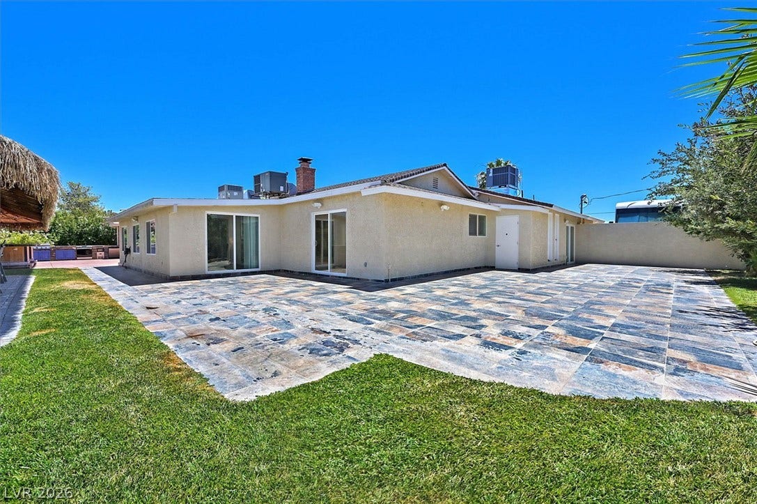 A spacious tiled patio expands behind a cream-colored stucco home, offering a perfect outdoor living space.