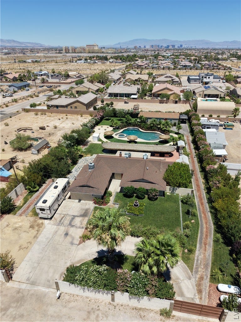 An aerial perspective reveals a private pool oasis amidst the desert landscape, framed by a spacious yard and distant mountains.