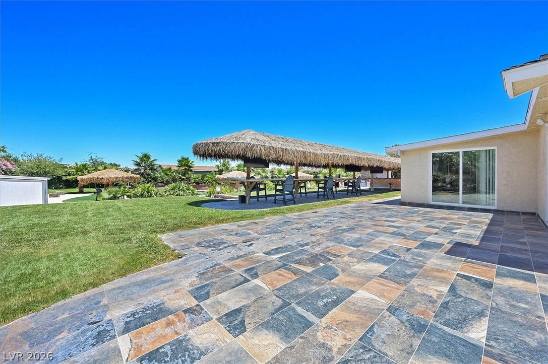 An inviting backyard oasis offers a spacious tiled patio leading to lush green lawn and an outdoor bar.