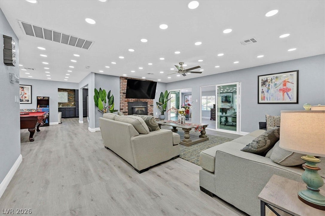 A spacious common area with a cozy fireplace, abundant recessed lighting, and a view of the outdoors.
