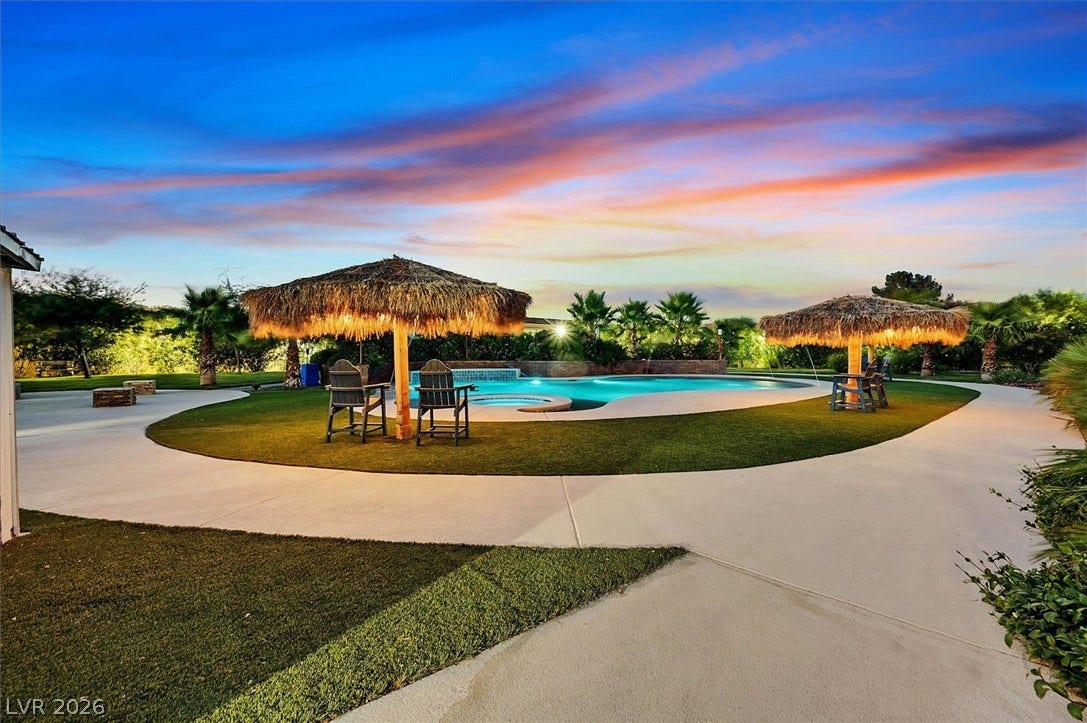 An inviting backyard oasis features a freeform pool with a spa, framed by lush landscaping and a tropical cabana.