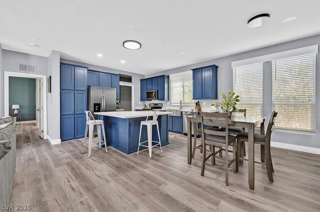 Bold blue cabinetry defines this naturally illuminated kitchen, featuring a spacious island and dining area.
