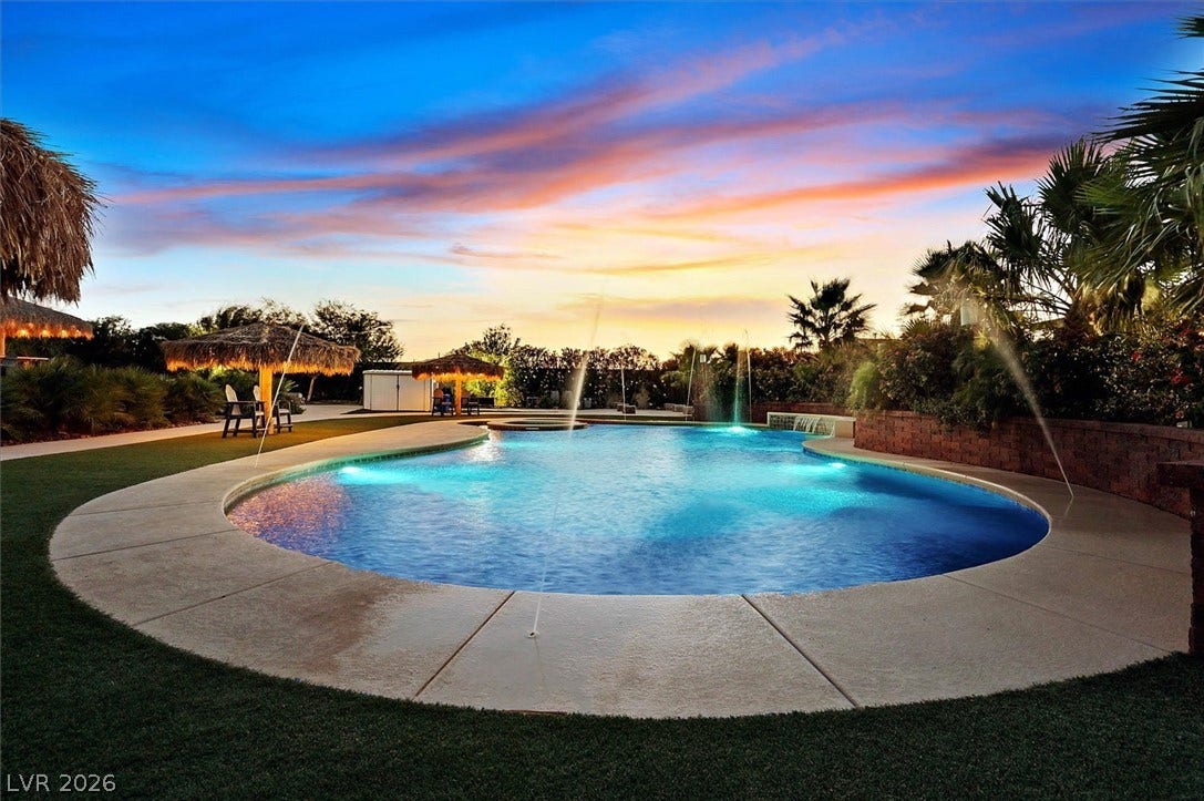 An inviting backyard oasis offers a sparkling pool with water features under a vibrant sunset.