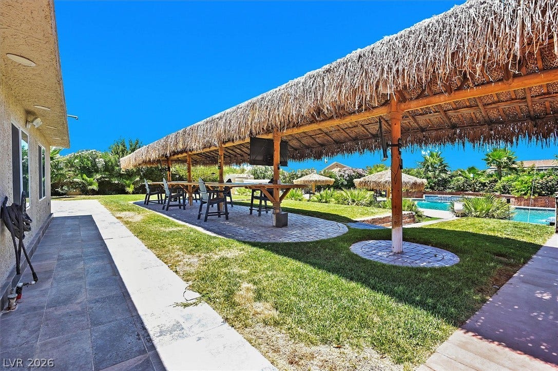 An inviting outdoor entertaining space features a long thatched-roof patio and an adjacent pool.