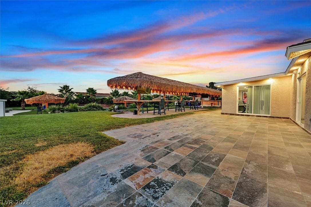 An inviting backyard oasis offers generous patio space and a spacious thatched-roof bar for entertaining.