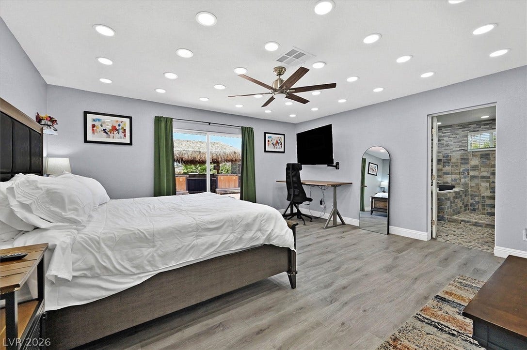 Recessed lighting and a ceiling fan illuminate this spacious primary bedroom featuring a glass door opening to outdoor relaxation.