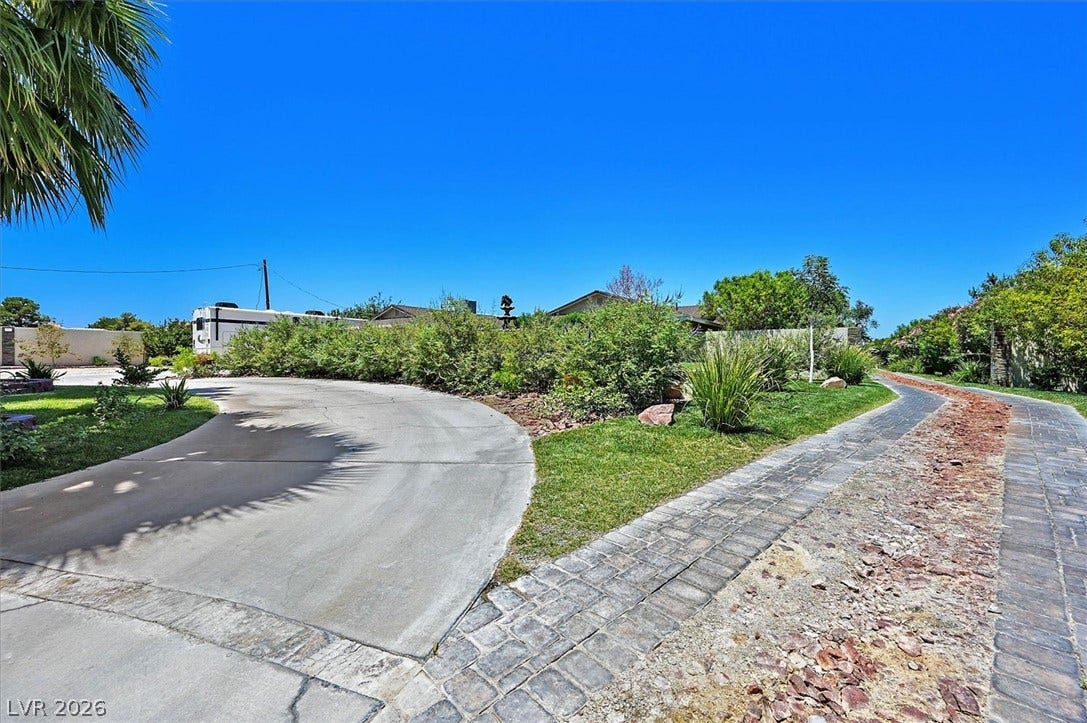 An inviting stone and concrete driveway winds through verdant landscaping toward the property.