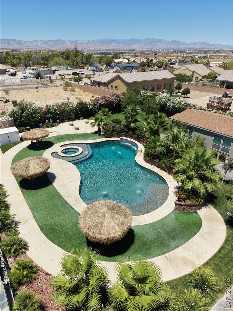 An aerial perspective reveals a sparkling free-form pool with an integrated spa, surrounded by lush landscaping and a manicured lawn.