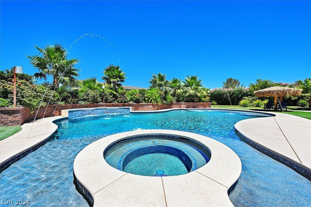 An inviting backyard oasis features a freeform pool with a built-in spa, surrounded by lush tropical landscaping.