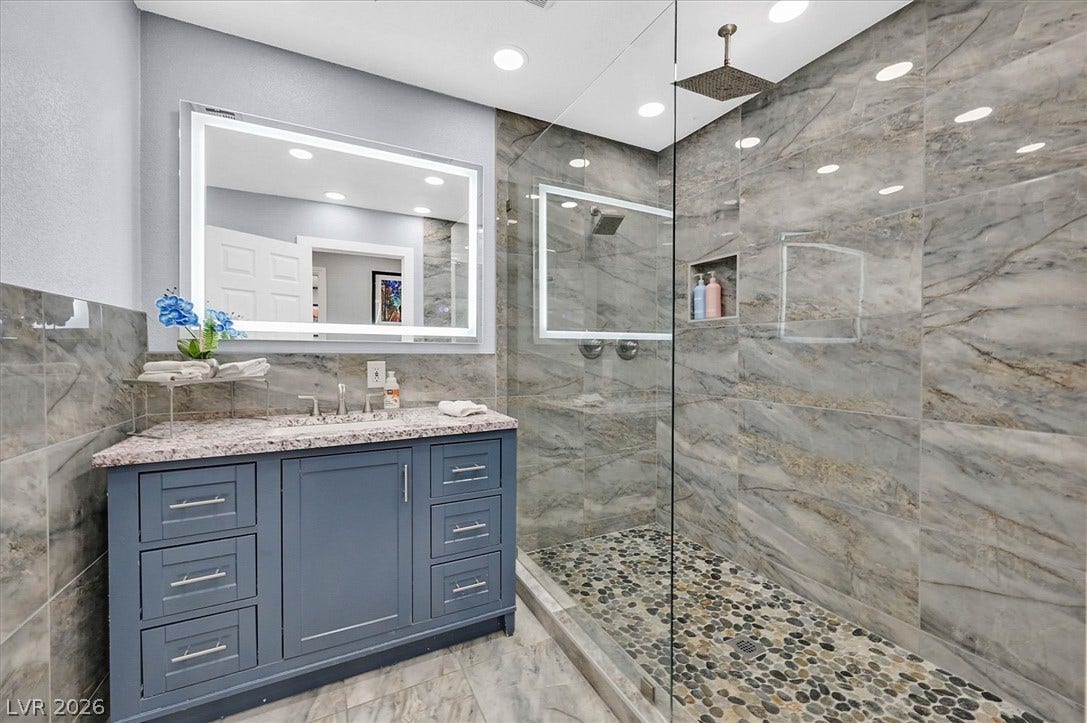 Modern bath offering a glass-enclosed shower with pebbled flooring and a sleek vanity with ample storage.