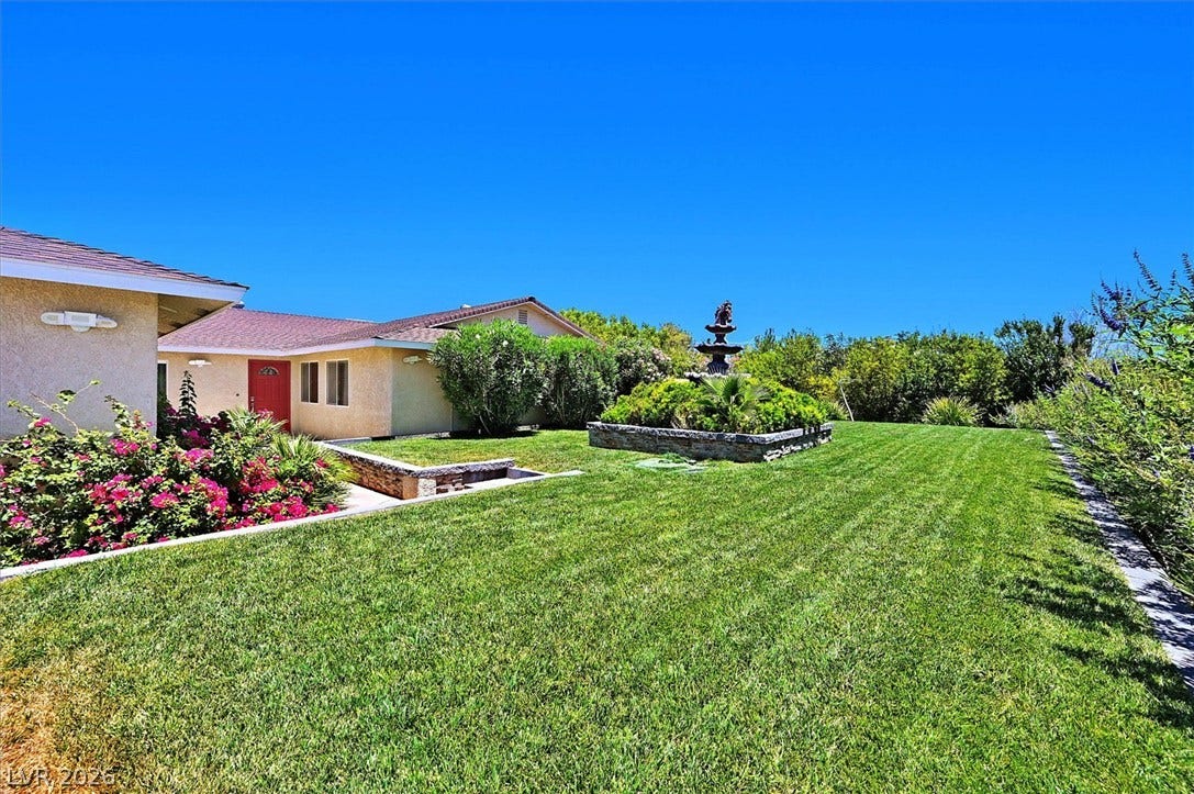 A vibrant green lawn and lush landscaping surround this charming property, featuring a decorative outdoor fountain.
