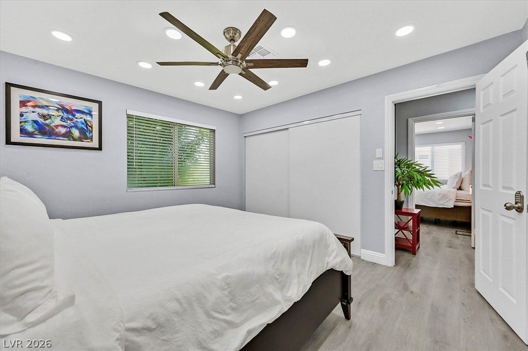 Recessed lighting and a stylish ceiling fan illuminate this well-appointed bedroom with light-toned flooring.