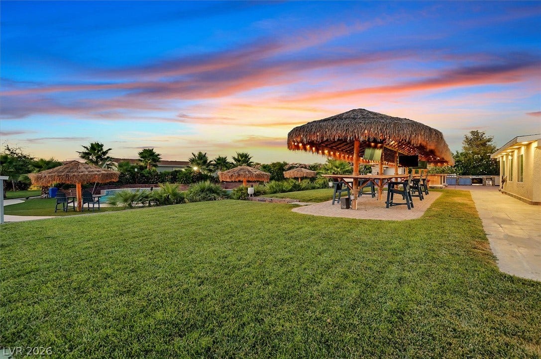 An inviting backyard oasis offers a tiki-style bar, ample lawn space, and a glistening pool.