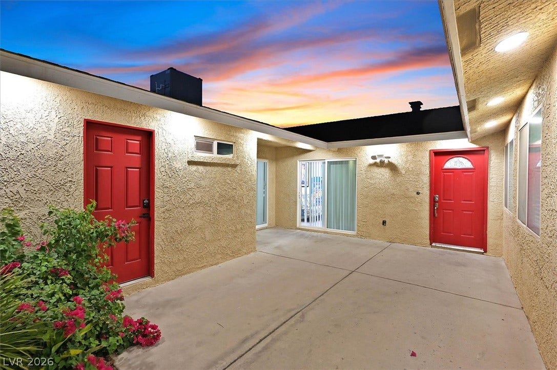Bold red doors punctuate the light stucco exterior, opening onto a clean concrete patio.