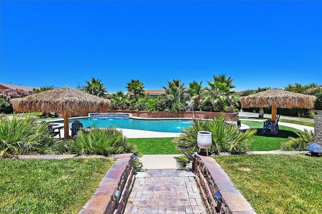 Tropical oasis featuring a sparkling pool, lush landscaping, and inviting thatched umbrellas for relaxation.