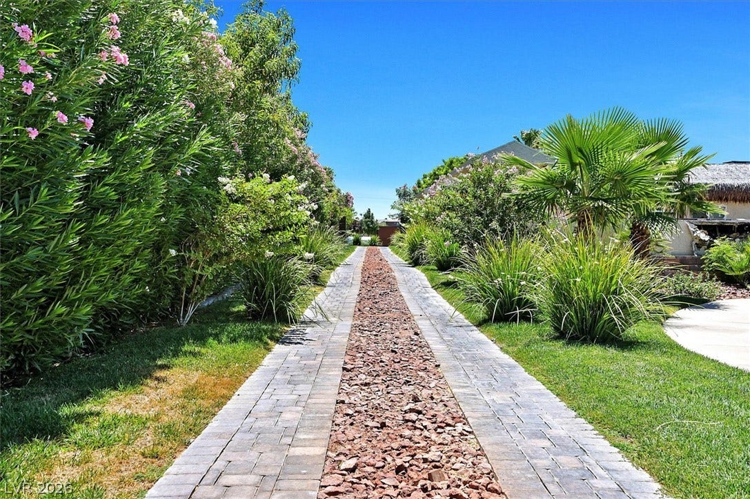 An inviting stone pathway, flanked by flourishing green foliage, leads to a private backyard retreat.