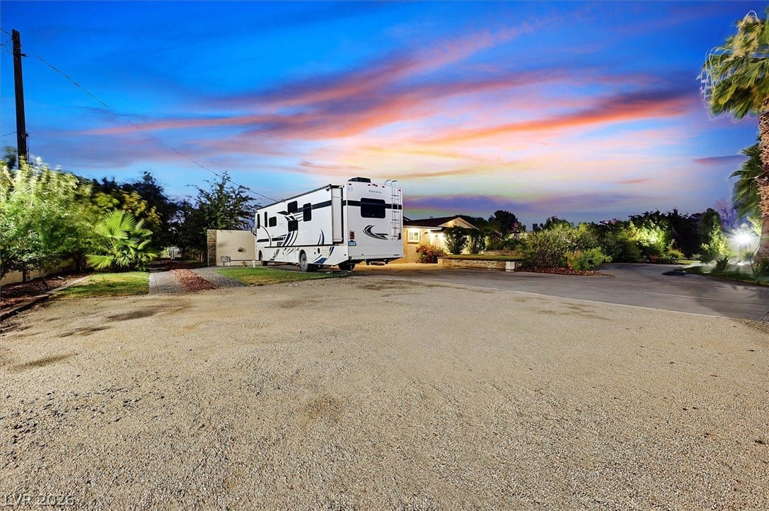 Dramatic sunset hues illuminate the spacious gravel driveway, offering ample parking and RV accommodation.