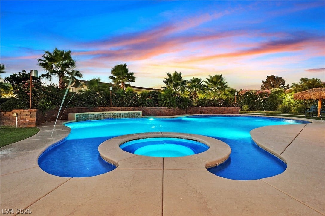 An inviting pool and spa glow under a colorful evening sky, nestled within a lush backyard oasis.