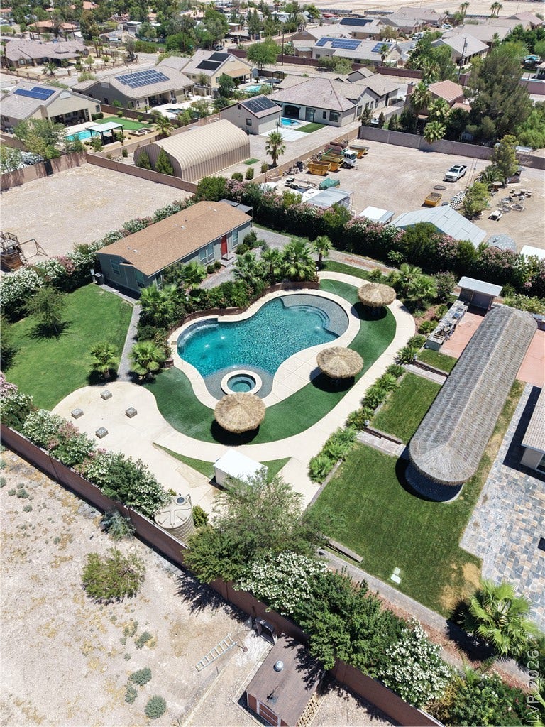 An aerial perspective reveals a sparkling pool, inviting patio, and lush green lawns amidst surrounding properties.