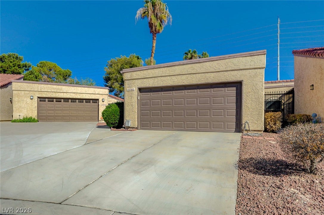 A spacious concrete driveway leads directly to the attached garage under clear blue skies.