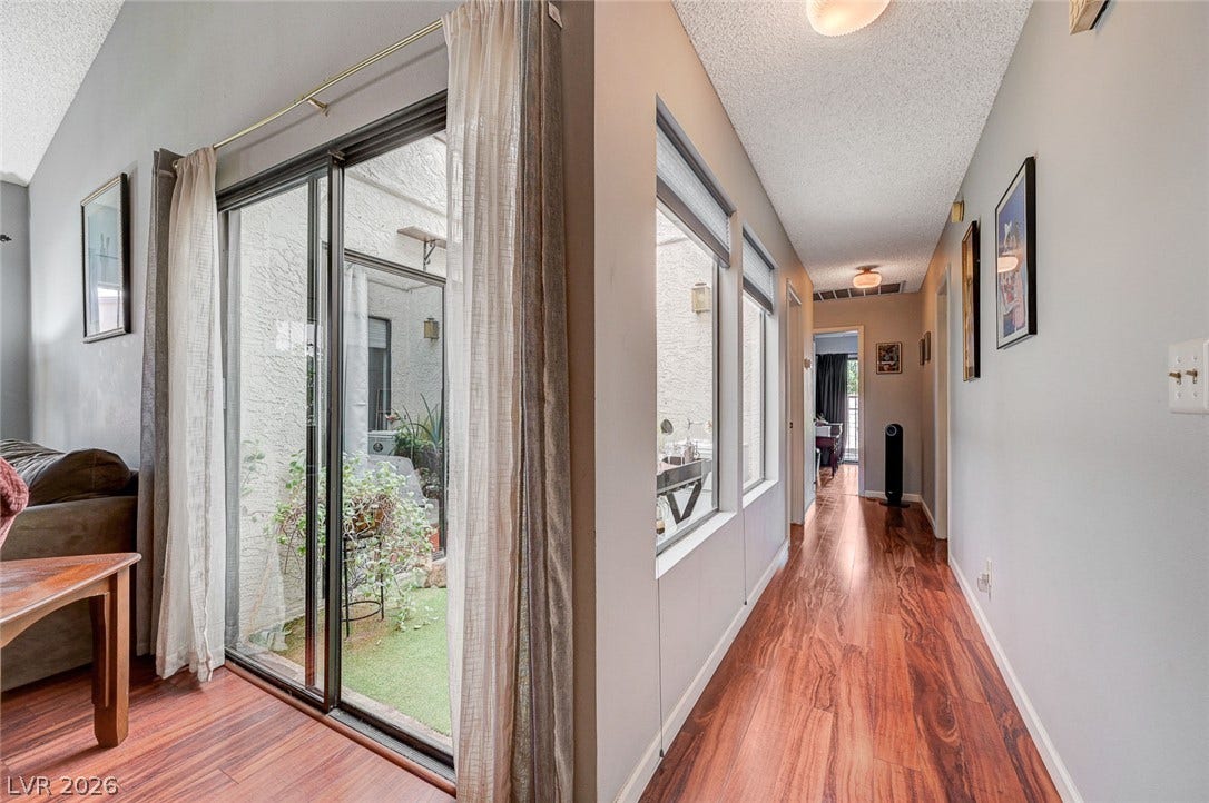 Rich wood flooring runs through a bright hallway lined with large windows.