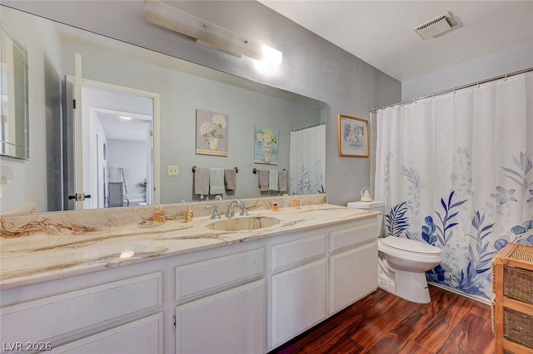 Richly veined stone countertops and warm wood floors elevate this well-appointed bathroom.