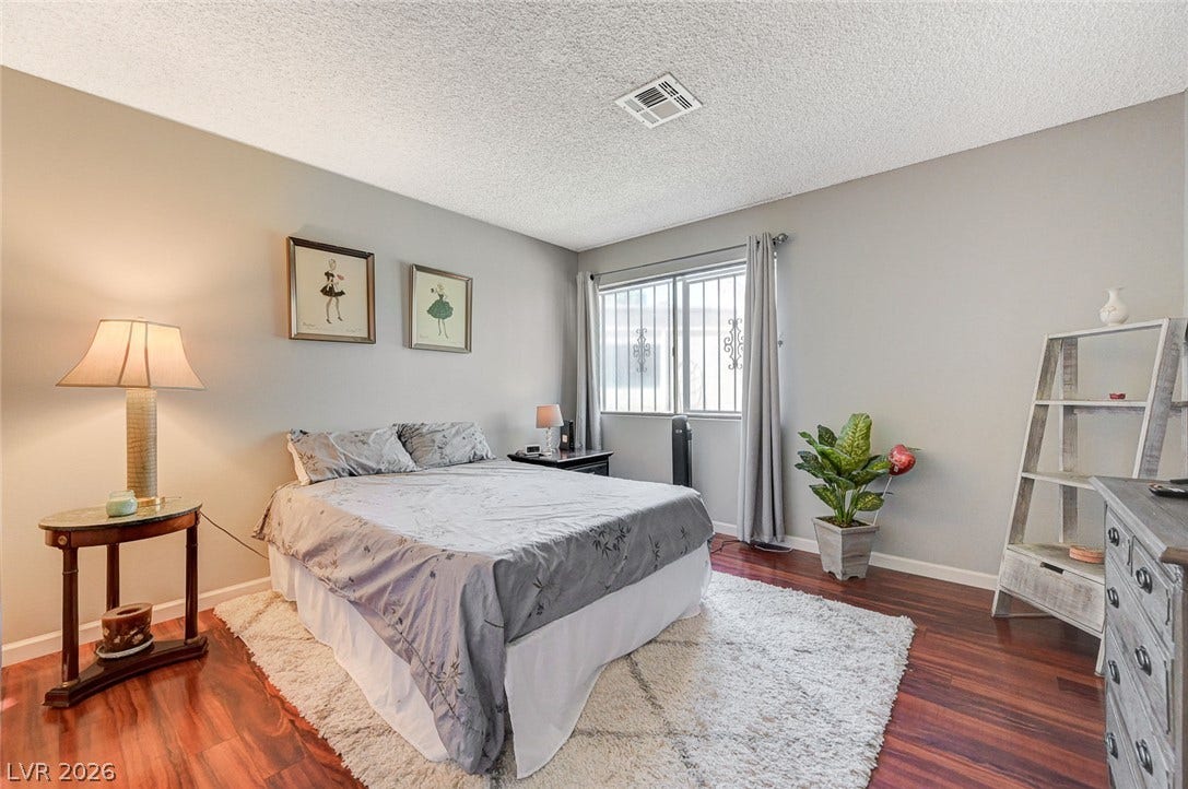 Rich hardwood flooring anchors this cozy bedroom under a textured ceiling with classic window details.
