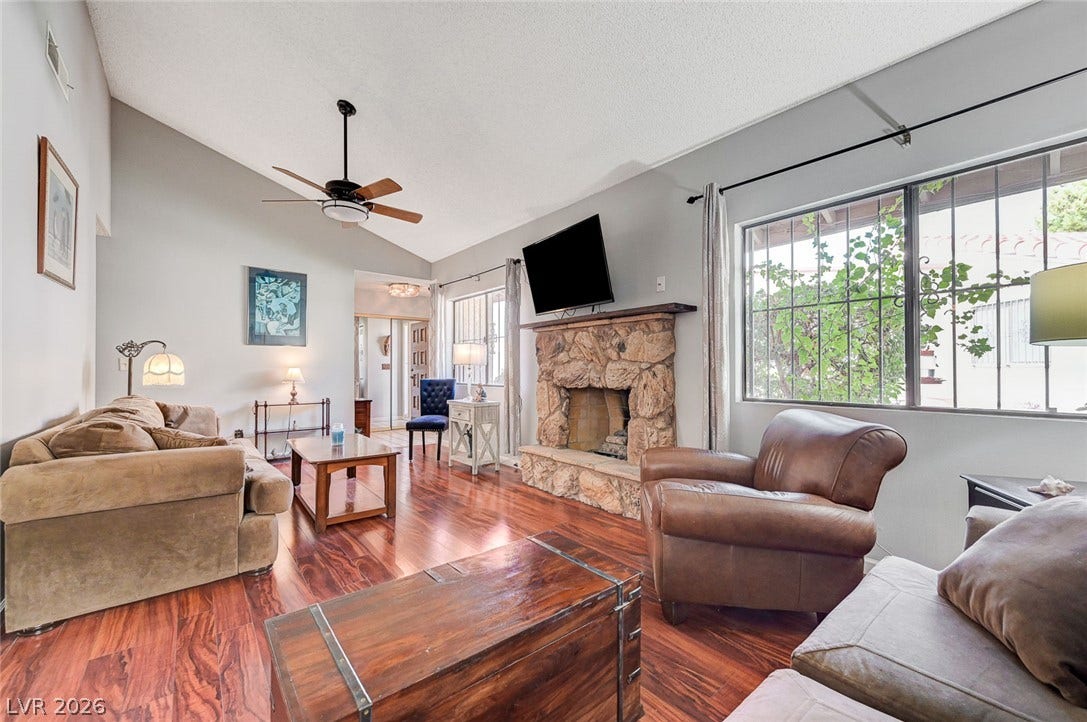 Rich hardwood flooring complements a robust stone fireplace beneath a soaring vaulted ceiling.