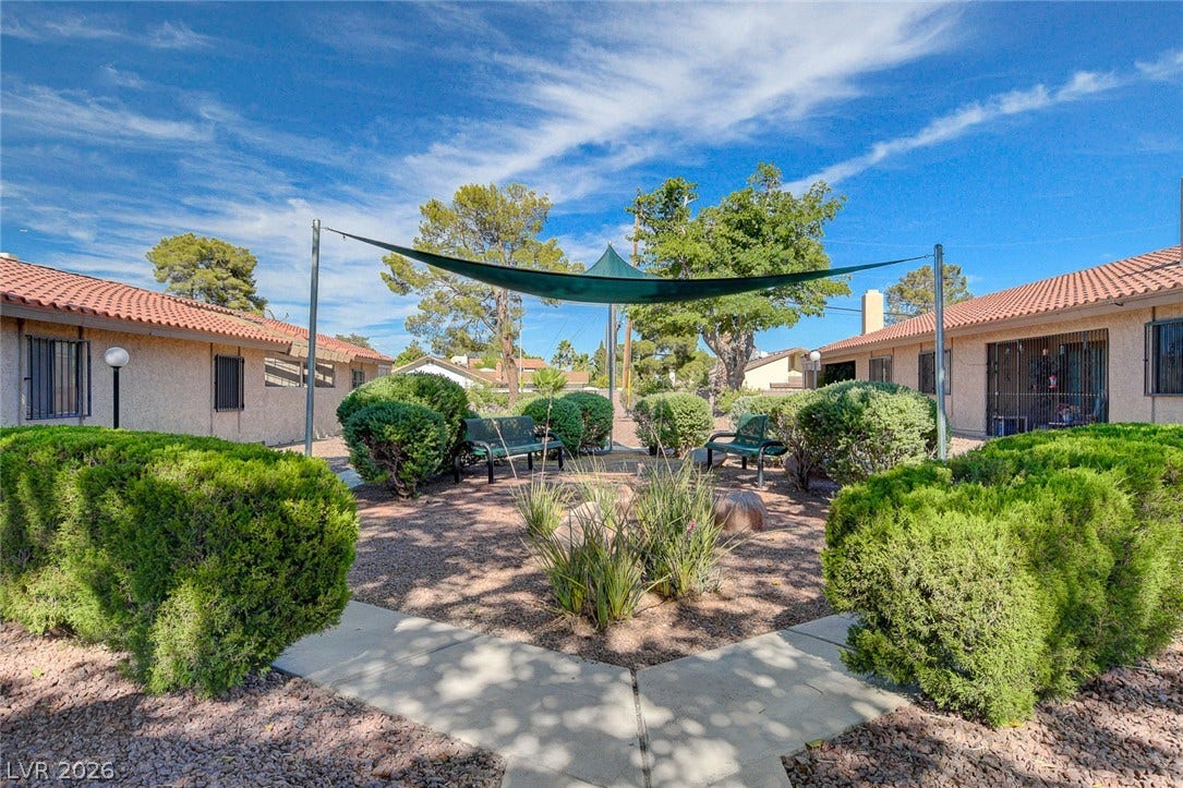 Manicured hedges flank concrete pathways leading toward a central shaded seating courtyard.
