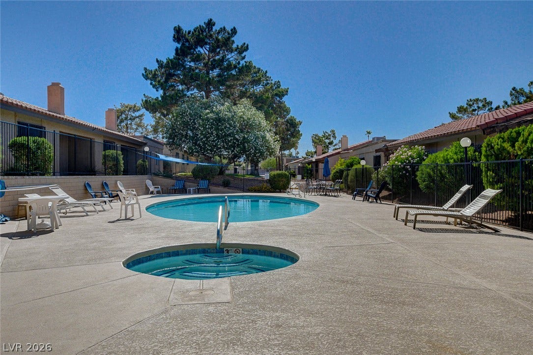 A sparkling community pool and spa are surrounded by a concrete deck and wrought iron fencing.