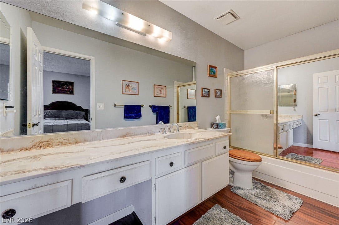 Rich wood flooring grounds this bathroom featuring an expansive vanity and built-in glass shower enclosure.