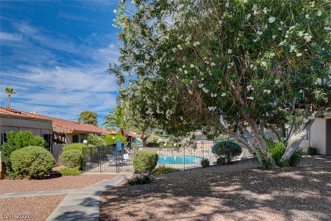 Mature trees and paved walkways frame a view of the community pool area.