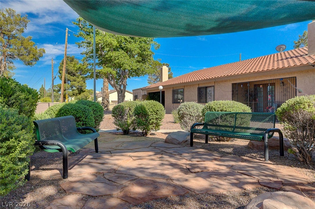 A stone patio provides a shaded outdoor space alongside low-maintenance landscaping and tile roof architectural elements.