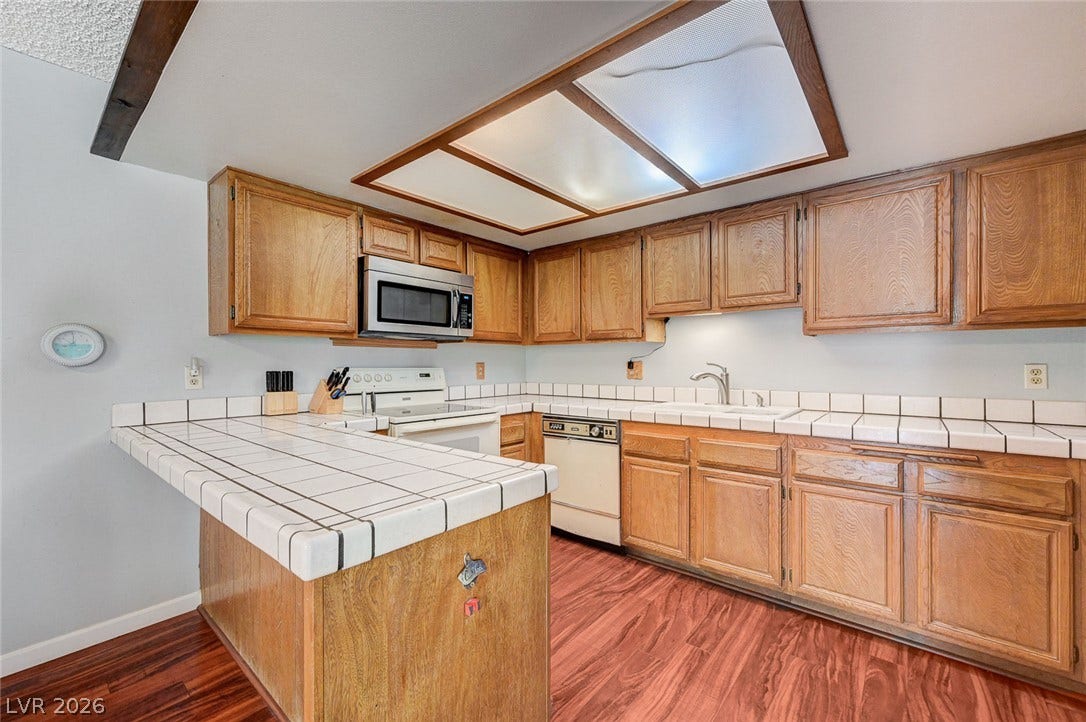 Rich wood floors complement classic cabinetry and tiled countertops in this traditional kitchen layout.