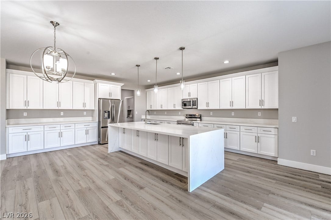 Kitchen with white cabinets, appliances with stainless steel finishes, light stone countertops, a spacious island, and light wood finished floors