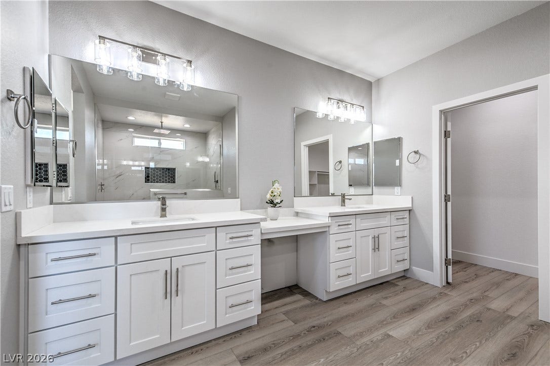 Full bath with two vanities, a marble finish shower, and light wood-style floors