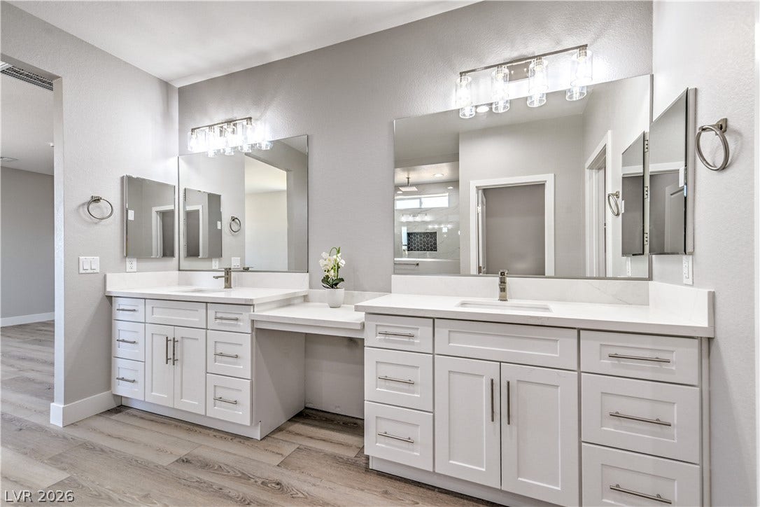 Full bath with a textured wall, two vanities, and light wood-style flooring