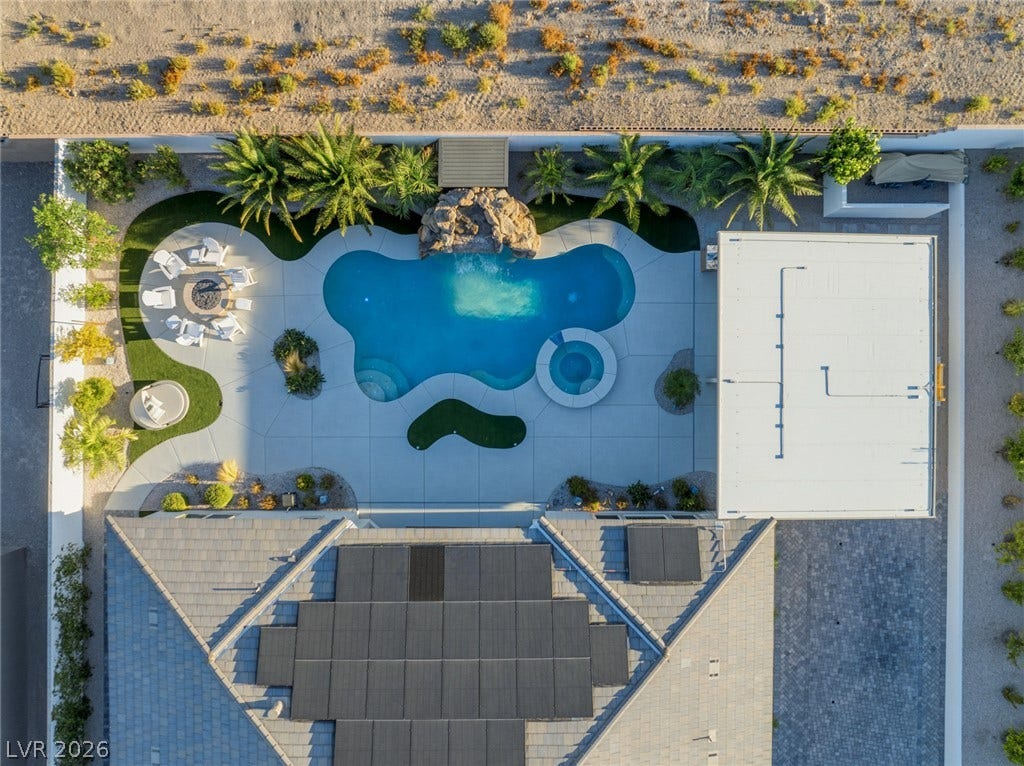An aerial view showcases a custom swimming pool surrounded by clean concrete decking and palms.