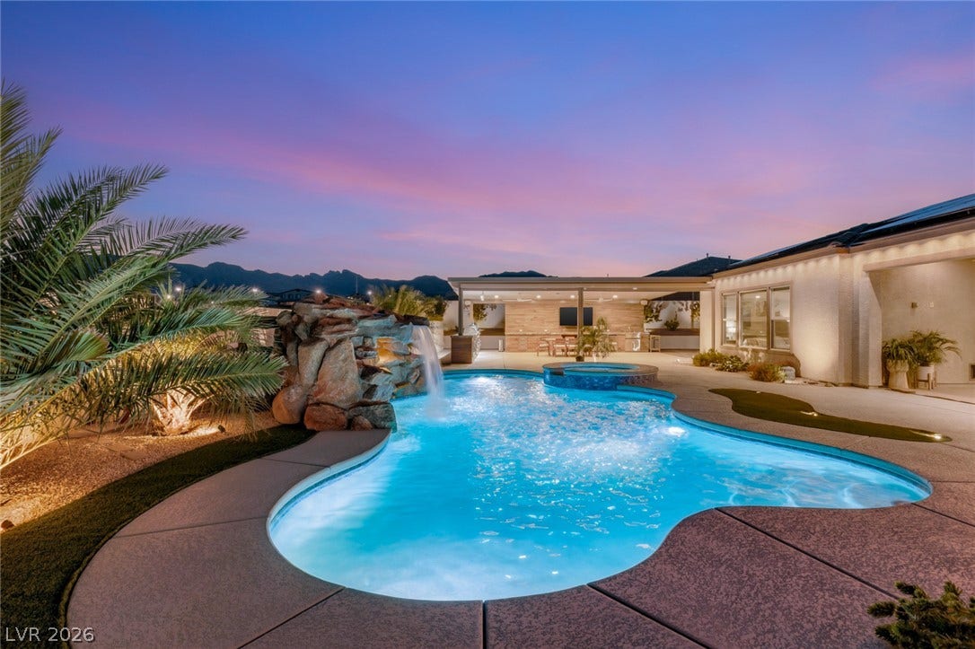 An inviting backyard pool showcases a stone waterfall feature against a scenic mountain backdrop.