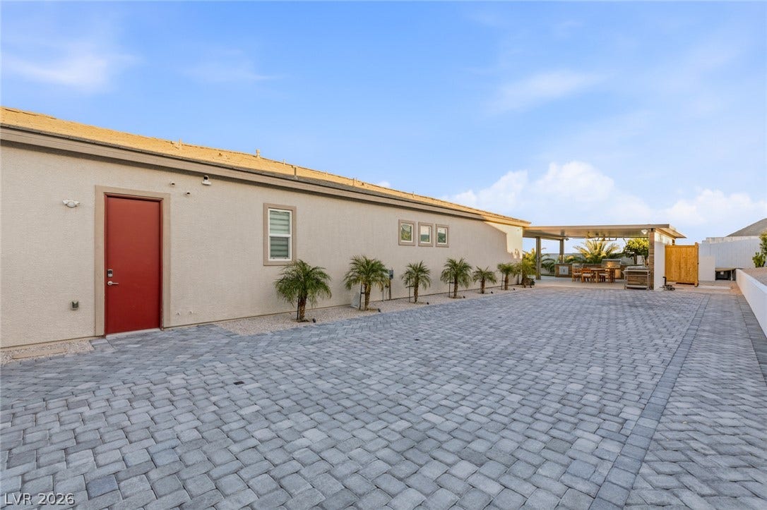 Expansive paver courtyard leads toward a covered outdoor kitchen and dining patio.