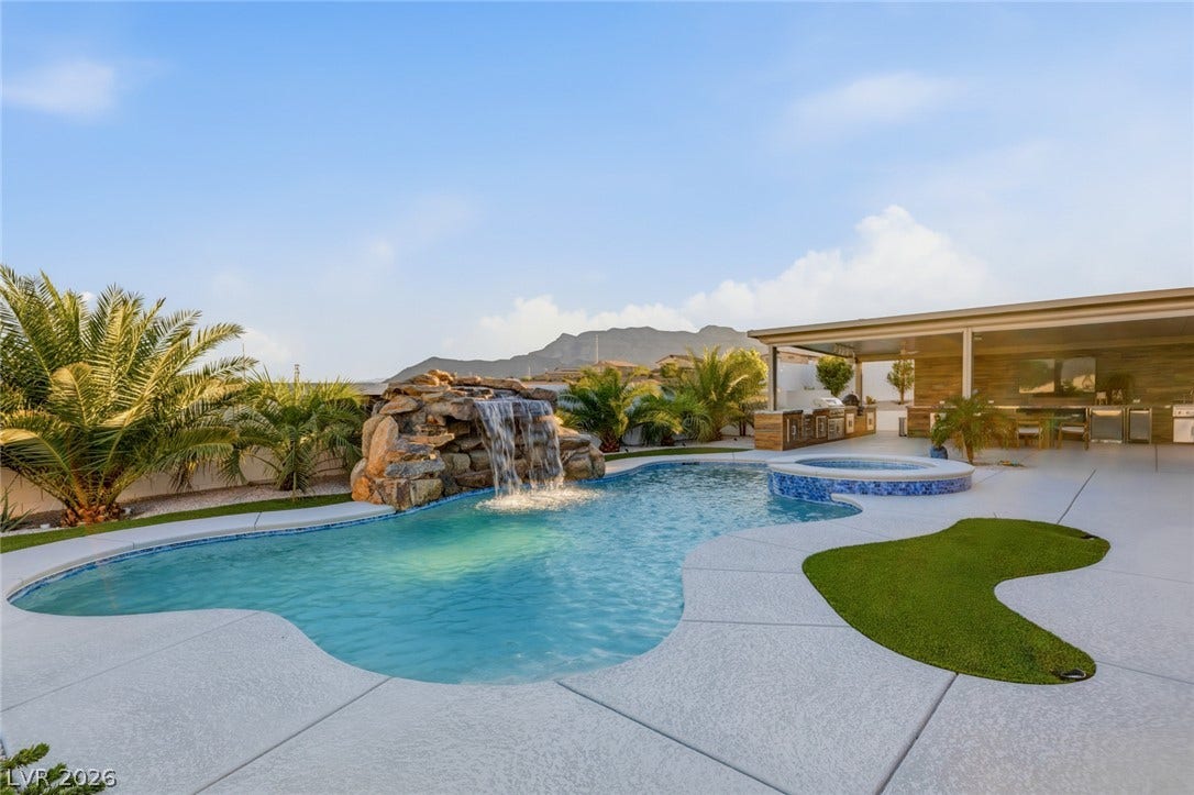 An inviting backyard pool features a cascading rock waterfall and integrated spa under clear skies.