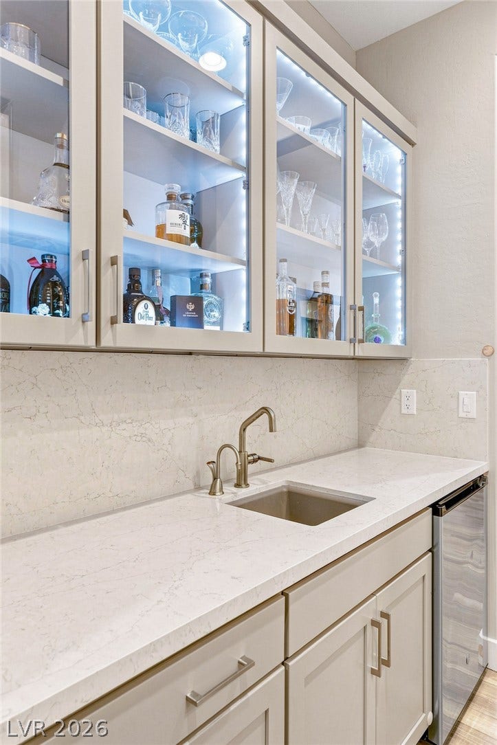 An elegant home bar features custom illuminated glass cabinets and smooth stone countertops.